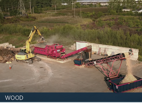 Exterior - High angle long view of an excavator dropping mattress wood into a woodchipper.